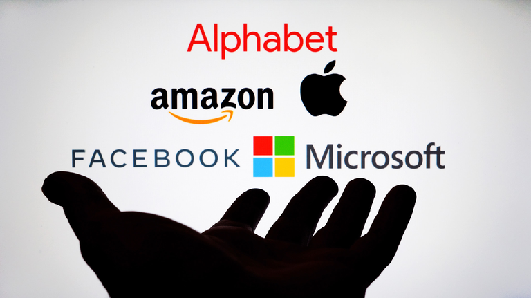 Silhouette of a hand reaching toward Alphabet, Amazon, Apple, Facebook and Microsoft logos