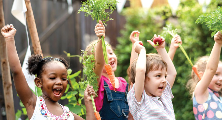 Children in a garden raising harvested vegetables above their heads