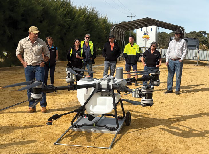 A group of growers standing around and closely examining the DJI T100 drone parked on the ground