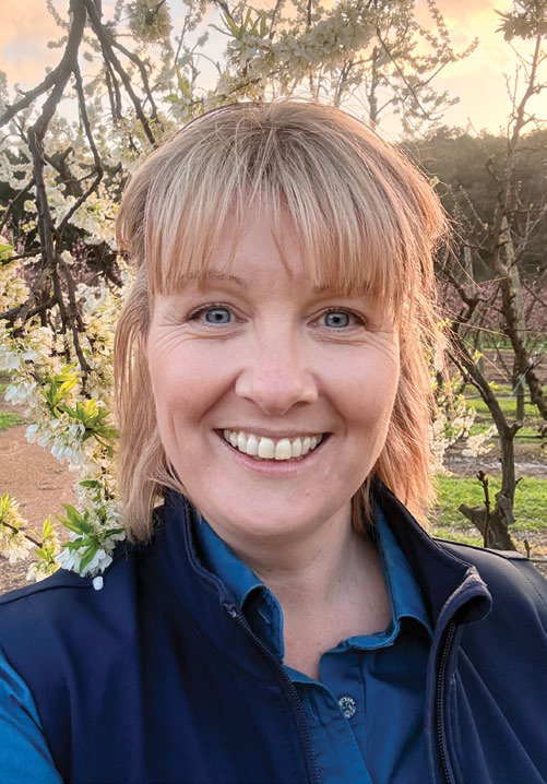 Kim Starkie standing among blossoming stonefruit trees