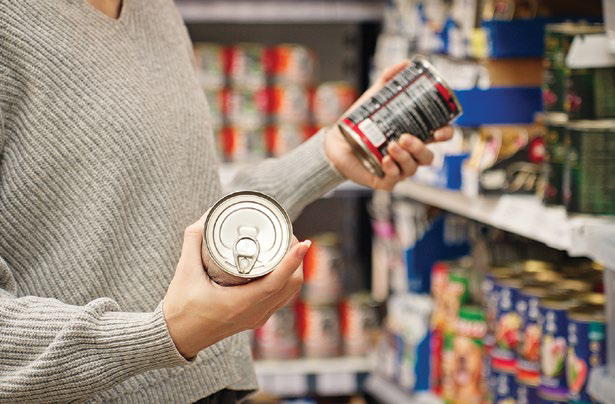 Person holding canned goods in a supermarket aisle