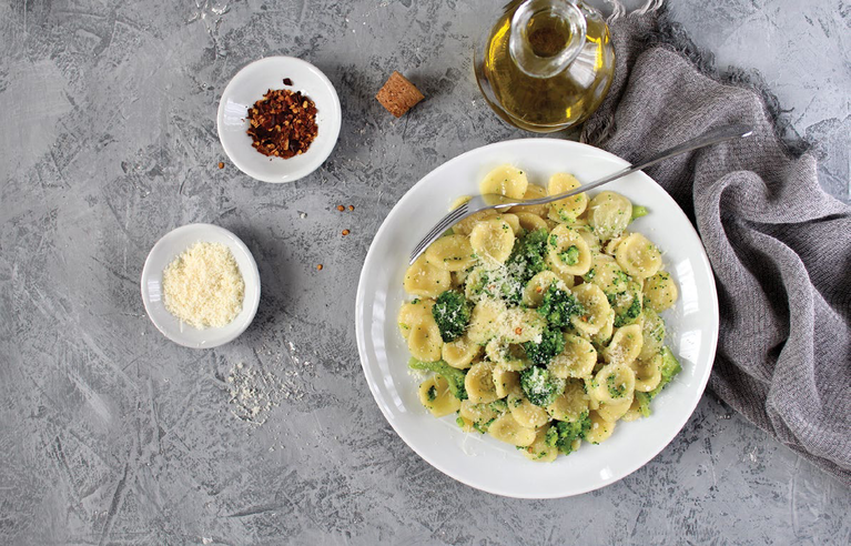 Broccoli pesto orecchiette pasta on a white plate with olive oil and chili flakes