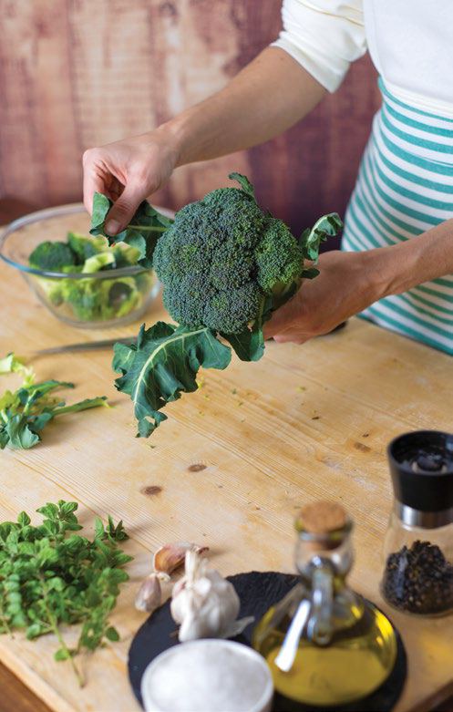 Hands holding fresh broccoli and preparing pesto ingredients on a wooden table