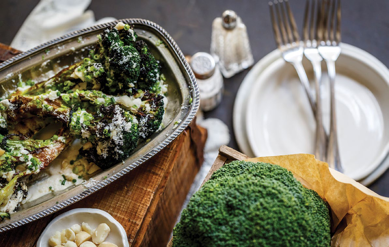 Roasted broccoli with macadamia saffron sauce on a serving platter with cutlery and plates